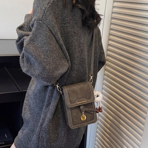 Detail view of small dark brown crossbody phone bag with gold lettering and plush charm