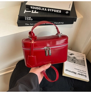 Detail of red glossy vanity case bag with silver dual zippers on a fashion book background