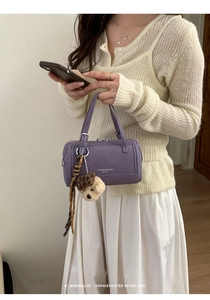 Détail du sac Boston violet avec boucles argentées, breloque chiot et pompon à rayures