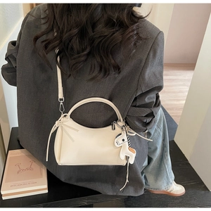 Detail of a beige half-moon handbag featuring a smooth matte finish and pony charm