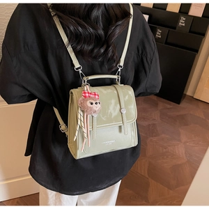 Detail of light green vintage leather backpack with plush monkey charm on back of model