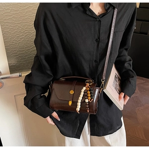Detail view of dark brown faux leather crossbody bag with beaded charm and metal buckle