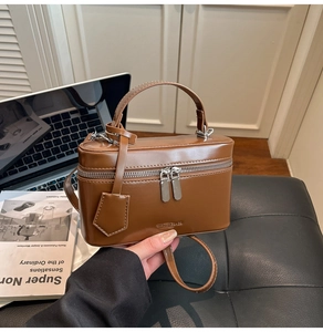 Detail of a brown matte leather box bag with dual zippers and branding in hand