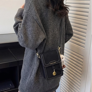 Detail of black crossbody phone bag with gold clasp and plush sheep charm on casual sweater