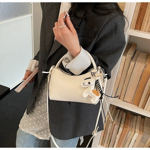 Elegante bolso bandolera blanco de media luna con colgante de caballo en estudio profesional
