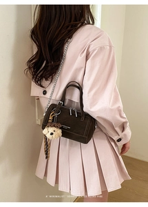 Détail du sac Boston marron foncé avec bandoulière chaîne et breloque ours sur modèle