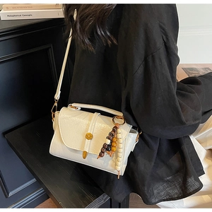 Detail of cream shoulder bag with wrinkled leather texture and beaded wood charm