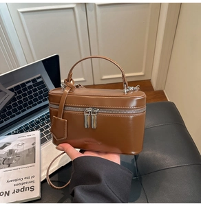 Close-up of brown leather box bag with silver zippers and adjustable shoulder strap