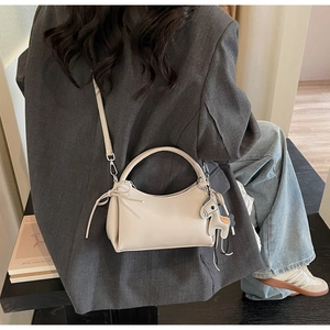 Detail of minimalist cream leather handbag featuring a decorative grey pony charm detail