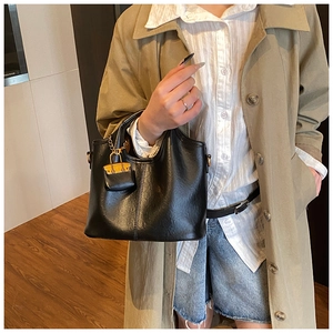 Détail d'un sac à main noir en simili cuir avec un mini charm jaune et des ferrures dorées