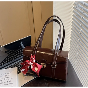 Détail macro du sac à main en cuir verni marron foncé brillant avec boucle dorée et foulard