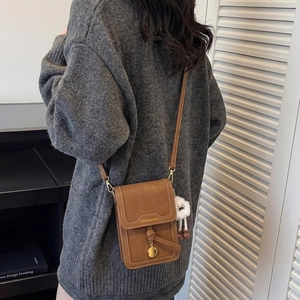 Detail view of brown matte leather crossbody phone bag with gold clasp and furry charm
