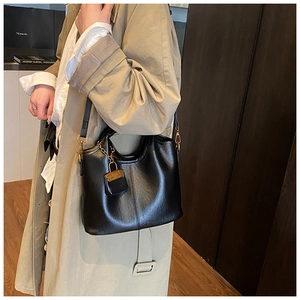 Sac à bandoulière en cuir noir avec breloque dorée porté sur un trench beige