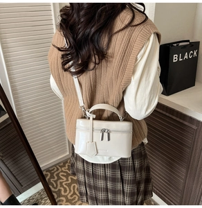 Model wearing a cream glossy leather box bag as a crossbody purse in a stylish room