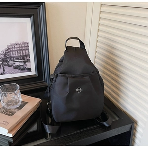 Dettaglio borsa a tracolla in nylon nero con logo in metallo su sfondo minimalista