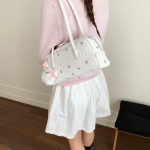 White shoulder bag with floral embroidery and a plush bunny charm on a model