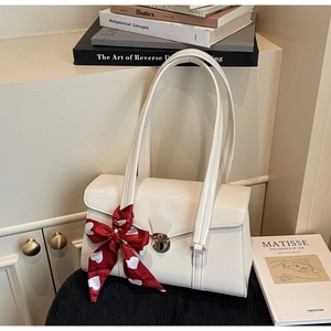 Gros plan d'un sac à rabat blanc avec boucle métallique et foulard en soie à cœurs rouges