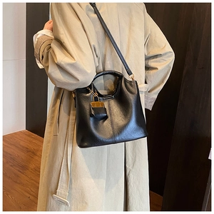 Détail d'un sac à main noir minimaliste porté à l'épaule avec un trench-coat classique
