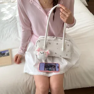 Detail of white floral shoulder bag with a cute plush puppy charm on a soft bed