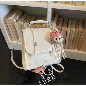 Detail of vintage beige backpack with buckle straps and a cute plush bear charm on shelf