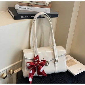 Détail d'un sac en cuir verni crème avec fermoir rotatif et foulard en soie rouge