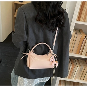 Pink minimalist crossbody bag with side bow detail and pony charm in bookstore setting