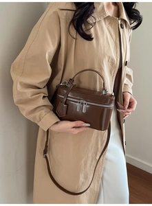 Detailed close-up of brown leather vanity bag with silver zippers and crossbody strap