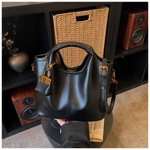 Détail d'un cabas en cuir noir avec chaîne dorée et mini pochette sur une chaise