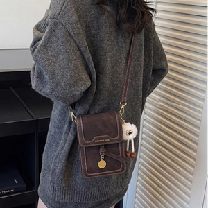 Close-up of brown crossbody bag with white stitching and plush charm on a model