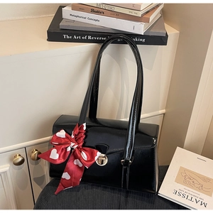 Détail du sac à bandoulière en vernis noir avec fermoir doré et foulard en soie à cœurs rouges