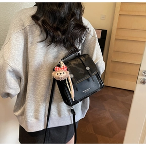 Detail view of black faux leather crossbody bag with buckle straps and plush charm