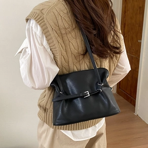 Detail of black pleated shoulder bag featuring a silver buckle on a model wearing beige