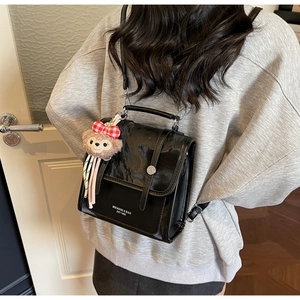 Detail of black patent leather backpack featuring a cute character plush charm and metal clasp