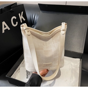 Dettaglio della borsa a secchiello in tela crema con tracolla in pelle e logo moda