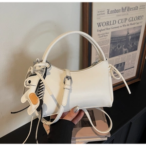 Detail of white half-moon leather bag with dog charm and adjustable shoulder strap