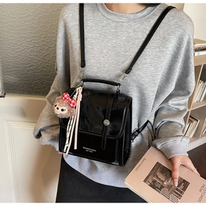 Detail of glossy black patent leather backpack with cute teddy bear charm accessory