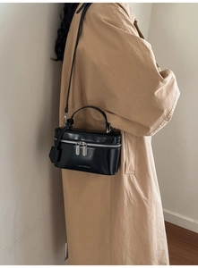 Detailed view of a black structured box bag with silver zippers and a top handle