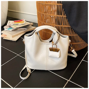 Détail d'un sac seau en cuir blanc avec coutures verticales et mini breloque de sac