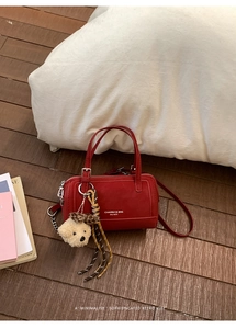 Vue détaillée d'un sac à main rouge mat avec breloque d'ours sur un parquet chaleureux