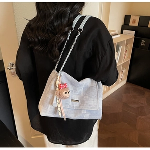 Dettaglio della borsa a tracolla a scacchi grigio-blu con placca in metallo e charm scimmia