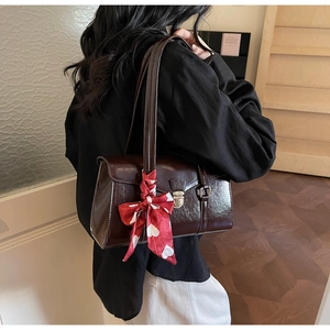 Détail du sac à main marron foncé brillant avec boucle en métal et foulard à cœurs