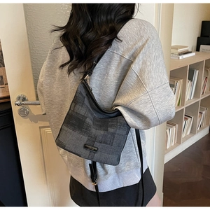 Dettaglio borsa a secchiello grigio scuro con motivi geometrici e targhetta in metallo