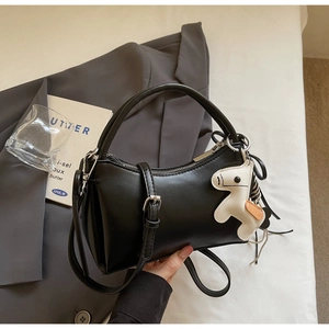 Detail of minimalist black leather handbag with a white horse charm and adjustable strap