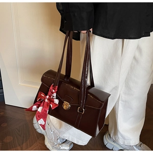 Détail d'un sac à main en cuir verni bordeaux avec fermoir métallique et foulard décoratif