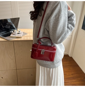 Close-up of a small red shiny leather box bag with silver zippers and a shoulder strap