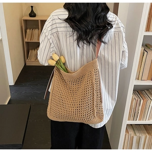 Detail of a khaki woven tote bag with leather strap worn by a model in a cozy study