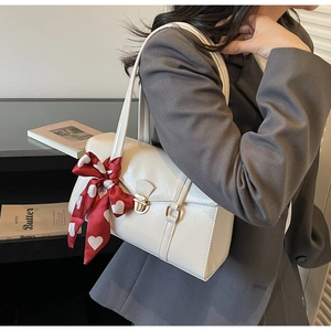 Gros plan sur un sac à bandoulière en cuir blanc avec fermoir doré et foulard à cœurs rouges
