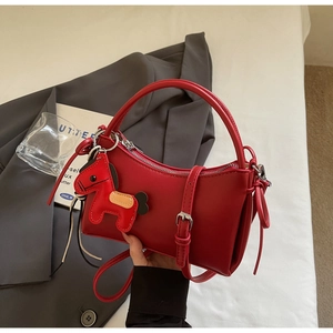 Detail of red synthetic leather hobo bag with silver buckle and horse charm on white sheets