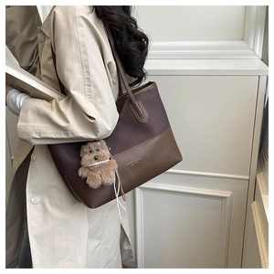 Dettaglio di una grande borsa tote marrone con ciondolo a orsetto e pelle patchwork