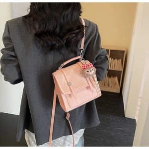 Detail of a pink glossy crossbody bag featuring a plush bear charm and brand logo